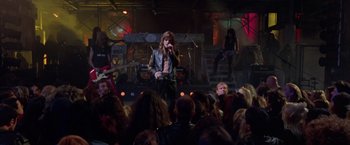 Movie still from “Rock Star” (2001), directed by Stephen Herek – A man in a leather jacket singing on a stage; Wide shot, High angle