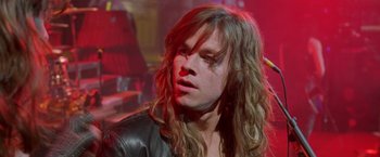 Movie still from “Rock Star” (2001), directed by Stephen Herek – A man with long blonde hair wearing a leather jacket; Close Up shot, Over the shoulder angle