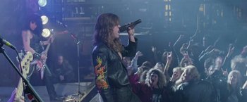 Movie still from “Rock Star” (2001), directed by Stephen Herek – A woman in a leather jacket singing into a microphone; Medium shot, Low angle