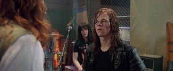 Movie still from “Rock Star” (2001), directed by Stephen Herek – A man with long black hair is standing in front of a microphone and another man with long black hair; Medium shot, Over the shoulder angle