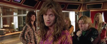 Movie still from “Rock Star” (2001), directed by Stephen Herek – A man with long brown hair wearing a purple shirt; Close Up shot, Over the shoulder angle
