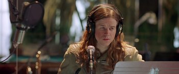 Movie still from “Rock Star” (2001), directed by Stephen Herek – A person wearing headphones and holding a microphone; Close Up shot, High angle