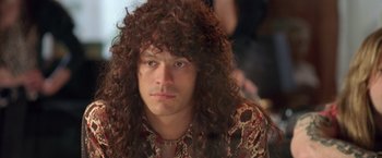 Movie still from “Rock Star” (2001), directed by Stephen Herek – A man with long curly brown hair wearing a shirt; Close Up shot, Over the shoulder angle