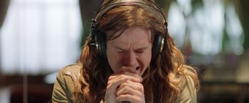 Movie still from “Rock Star” (2001), directed by Stephen Herek – A person with long hair wearing headphones and holding their hands to his mouth; Close Up shot, High angle