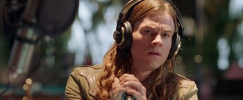 Movie still from “Rock Star” (2001), directed by Stephen Herek – A woman with long brown hair wearing headphones and holding a microphone; Close Up shot, High angle