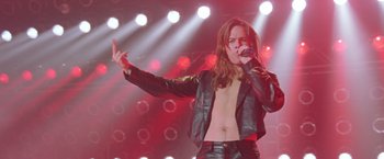 Movie still from “Rock Star” (2001), directed by Stephen Herek – A man in a leather jacket singing into a microphone on a stage; Medium shot, Low angle