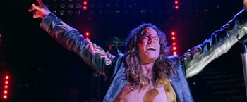 Movie still from “Rock Star” (2001), directed by Stephen Herek – A man with long curly hair is laughing and raising his arms; Medium shot, Low angle