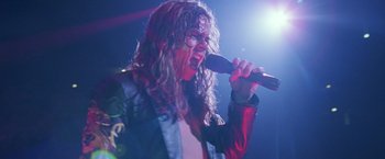 Movie still from “Rock Star” (2001), directed by Stephen Herek – A man with long hair and glasses is singing into a microphone; Close Up shot, Low angle