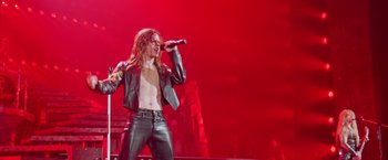 Movie still from “Rock Star” (2001), directed by Stephen Herek – A man in a leather jacket is holding a microphone; Medium shot, Low angle