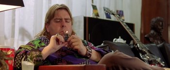 Movie still from “Rock Star” (2001), directed by Stephen Herek – A man smoking a cigarette while sitting on a couch; Medium shot, High angle