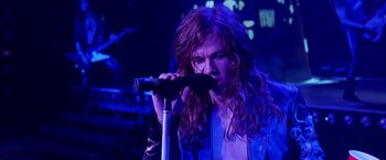 Movie still from “Rock Star” (2001), directed by Stephen Herek – A man with long hair is singing into a microphone; Close Up shot, High angle