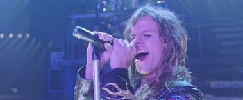 Movie still from “Rock Star” (2001), directed by Stephen Herek – A man with long brown hair is singing into a microphone; Close Up shot, Low angle