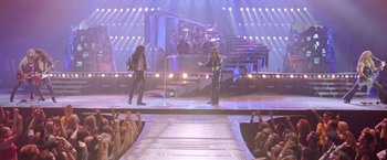 Movie still from “Rock Star” (2001), directed by Stephen Herek – A couple of men standing on top of a stage next to a crowd; Wide shot, High angle