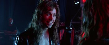 Movie still from “Rock Star” (2001), directed by Stephen Herek – A man with long brown hair smiles for the camera; Close Up shot, Over the shoulder angle