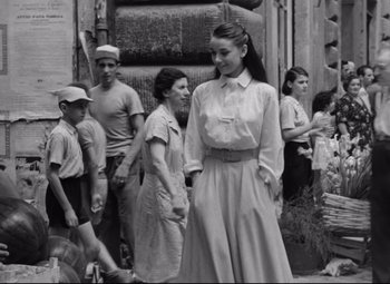 Movie still from “Roman Holiday” (1953), directed by William Wyler – An old photo of a woman standing in front of other people; Medium shot, Over the shoulder angle