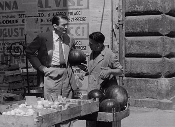 Movie still from “Roman Holiday” (1953), directed by William Wyler – Two men standing next to each other in front of a table; Medium shot, Low angle