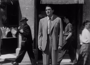 Movie still from “Roman Holiday” (1953), directed by William Wyler – A man in a suit and tie standing in front of a building; Medium shot, Low angle