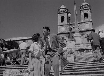 Movie still from “Roman Holiday” (1953), directed by William Wyler – A man and a woman standing next to each other on some steps; Wide shot, Low angle
