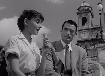 Movie still from “Roman Holiday” (1953), directed by William Wyler – A man and a woman standing next to each other in front of a clock tower; Medium shot, Low angle