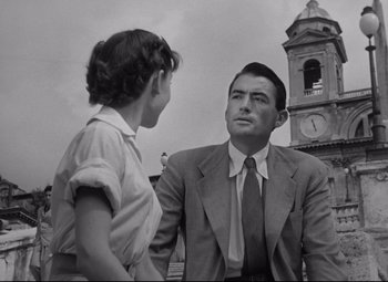 Movie still from “Roman Holiday” (1953), directed by William Wyler – A man and a woman are standing in front of a clock tower; Medium shot, Low angle