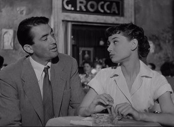 Movie still from “Roman Holiday” (1953), directed by William Wyler – A man and a woman sitting at a table in a restaurant; Medium shot, Over the shoulder angle
