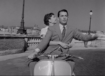 Movie still from “Roman Holiday” (1953), directed by William Wyler – A man and a woman riding a scooter on a street; Medium shot, Low angle
