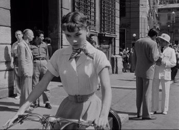 Movie still from “Roman Holiday” (1953), directed by William Wyler – A woman riding a bike down a street; Medium shot, Over the shoulder angle