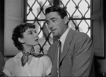 Movie still from “Roman Holiday” (1953), directed by William Wyler – A man and a woman standing next to each other in front of a window; Medium shot, Low angle