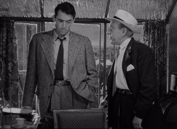 Movie still from “Roman Holiday” (1953), directed by William Wyler – A man and a man in a suit standing next to each other; Medium shot, Over the shoulder angle