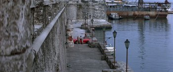 Movie still from “Romancing the Stone” (1984), directed by Robert Zemeckis – Two people are sitting on a pier next to a body of water; Extreme Wide shot, High angle