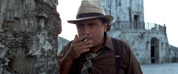 Movie still from “Romancing the Stone” (1984), directed by Robert Zemeckis – A man in a hat smoking a cigarette next to a tree; Close Up shot, Low angle