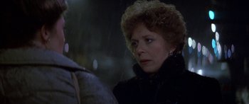 Movie still from “Romancing the Stone” (1984), directed by Robert Zemeckis – An older woman in a black jacket looking at the camera; Close Up shot, Over the shoulder angle