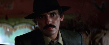 Movie still from “Romancing the Stone” (1984), directed by Robert Zemeckis – A person wearing a hat and a suit; Close Up shot, Low angle