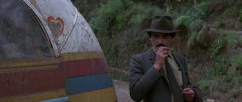 Movie still from “Romancing the Stone” (1984), directed by Robert Zemeckis – A man in a fedora smoking a cigarette; Medium shot, Over the shoulder angle