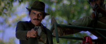 Movie still from “Romancing the Stone” (1984), directed by Robert Zemeckis – A man in a hat and tie holding a gun; Close Up shot, Low angle