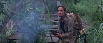 Movie still from “Romancing the Stone” (1984), directed by Robert Zemeckis – A man holding a gun while standing next to a bush; Medium shot, Low angle