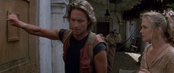 Movie still from “Romancing the Stone” (1984), directed by Robert Zemeckis – A man with long blonde hair is walking; Close Up shot, Over the shoulder angle