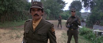 Movie still from “Romancing the Stone” (1984), directed by Robert Zemeckis – A group of men standing on top of a grass covered field; Medium shot, Low angle