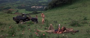 Movie still from “Romancing the Stone” (1984), directed by Robert Zemeckis – A group of people sitting in the grass near a car; Wide shot, Low angle