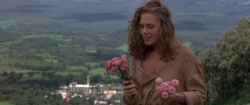 Movie still from “Romancing the Stone” (1984), directed by Robert Zemeckis – A beautiful woman holding a bunch of pink flowers; Medium shot, Over the shoulder angle