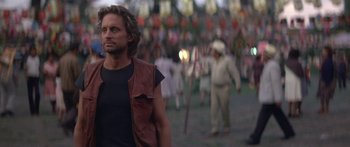 Movie still from “Romancing the Stone” (1984), directed by Robert Zemeckis – A man in a leather vest walks through a crowd of people; Close Up shot, Over the shoulder angle