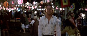 Movie still from “Romancing the Stone” (1984), directed by Robert Zemeckis – A man in a white shirt is standing in a crowd; Close Up shot, Low angle