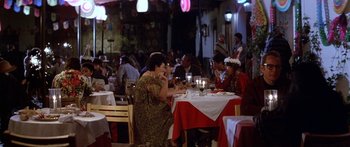 Movie still from “Romancing the Stone” (1984), directed by Robert Zemeckis – A group of people sitting at a table with food on it; Wide shot, High angle