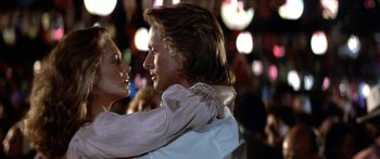 Movie still from “Romancing the Stone” (1984), directed by Robert Zemeckis – A man and a woman are hugging in front of lights; Close Up shot, Low angle