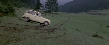 Movie still from “Romancing the Stone” (1984), directed by Robert Zemeckis – An old car is parked in the middle of a grassy field; Extreme Wide shot, High angle