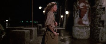 Movie still from “Romancing the Stone” (1984), directed by Robert Zemeckis – A woman walking down a street at night with a bag; Medium shot, Over the shoulder angle