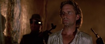Movie still from “Romancing the Stone” (1984), directed by Robert Zemeckis – A man with a gun standing next to another man; Close Up shot, Over the shoulder angle