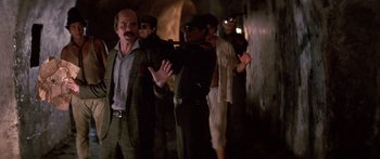 Movie still from “Romancing the Stone” (1984), directed by Robert Zemeckis – A group of men standing next to each other in a tunnel; Medium shot, Over the shoulder angle