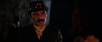 Movie still from “Romancing the Stone” (1984), directed by Robert Zemeckis – A man in a uniform and a hat is standing in the dark; Close Up shot, Over the shoulder angle