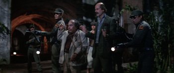 Movie still from “Romancing the Stone” (1984), directed by Robert Zemeckis – A group of men standing next to each other on a street; Medium shot, Low angle